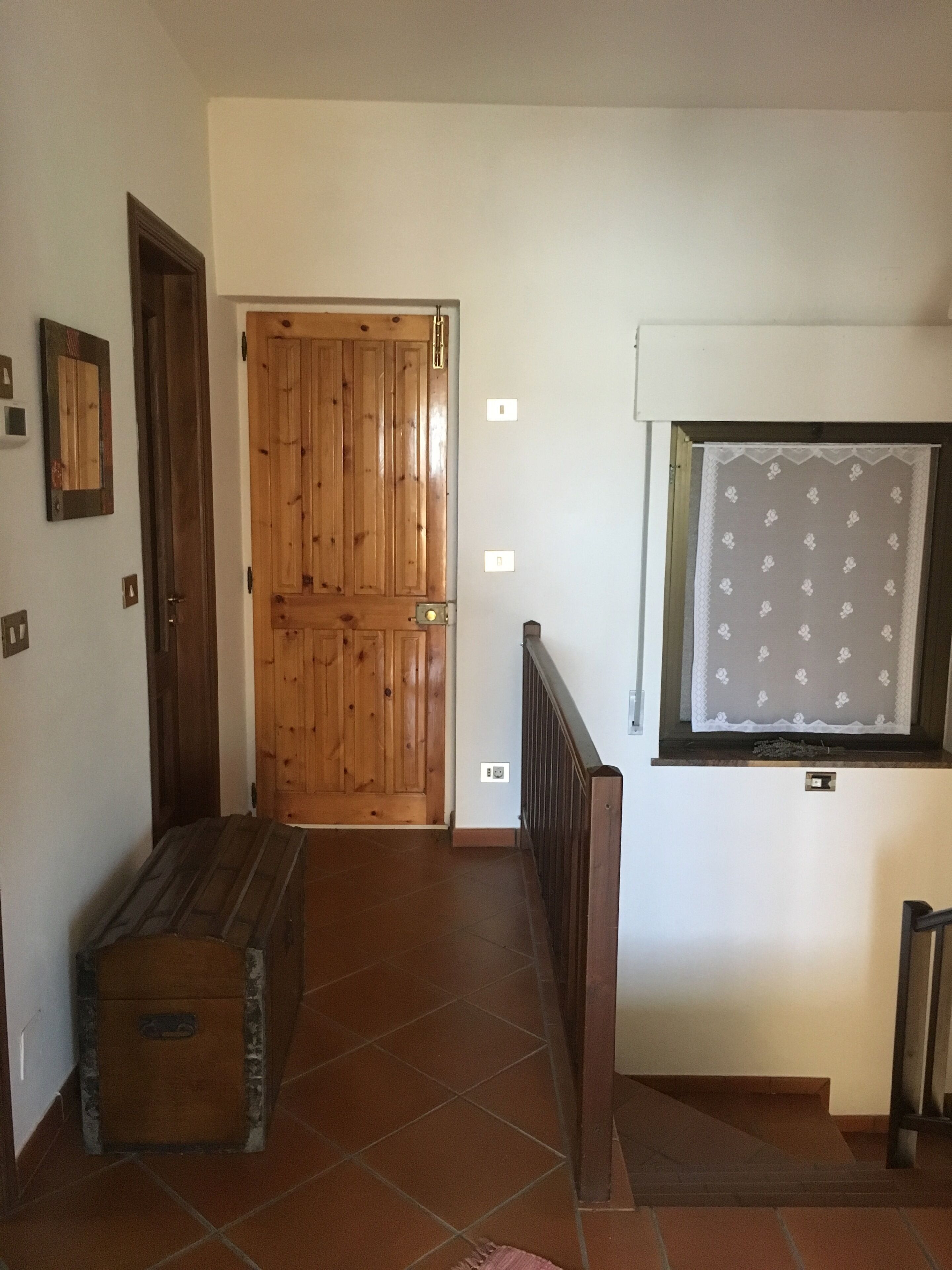 Un pasillo con una puerta de madera, un banco y una ventana con cortina estampada.