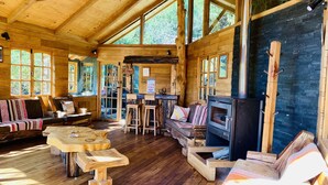 A rustic wooden cabin interior with a fireplace, wooden furniture, and large windows.