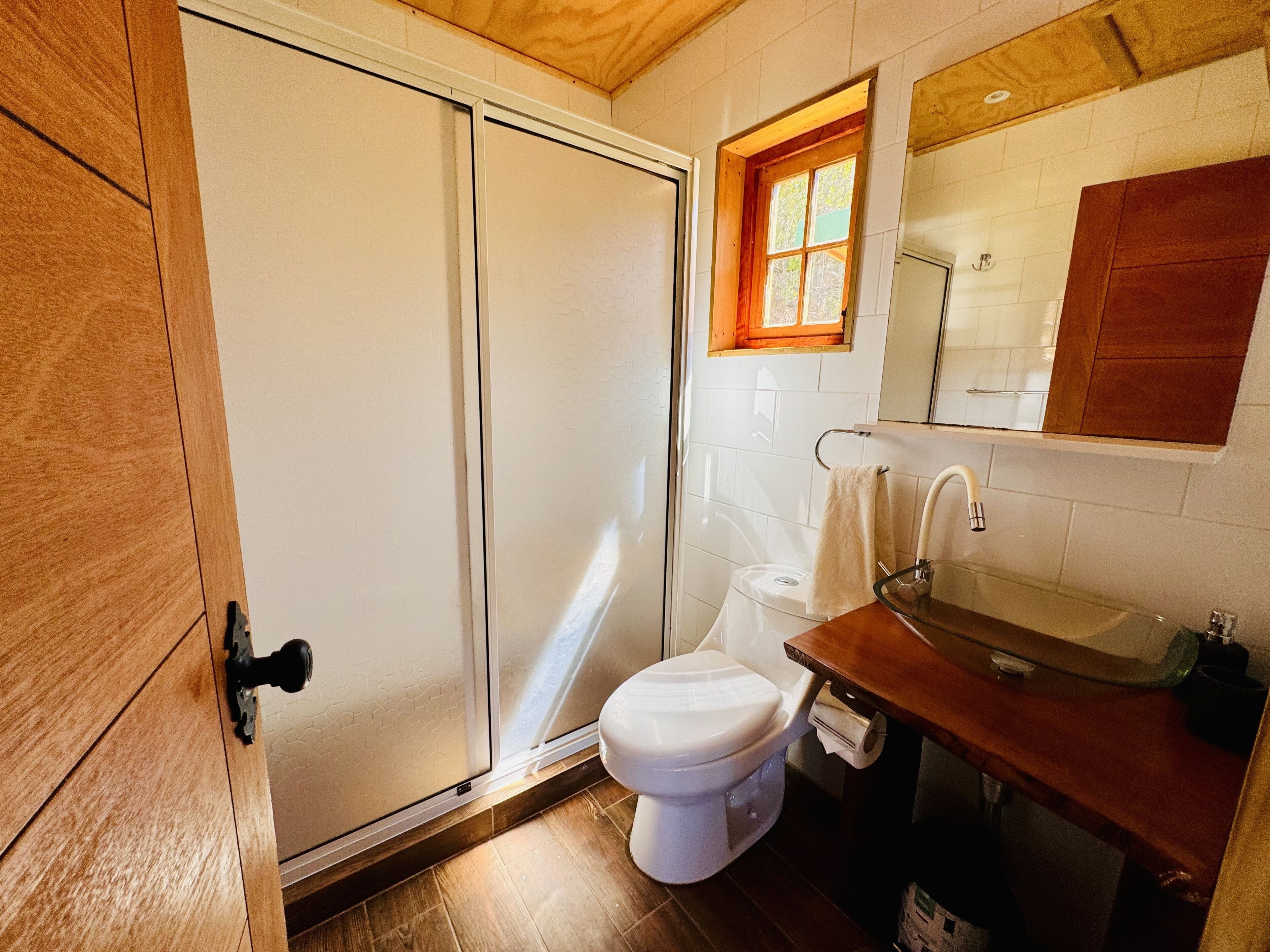 Un baño con puerta de madera, un inodoro, un lavabo y una ventana sobre el lavabo.