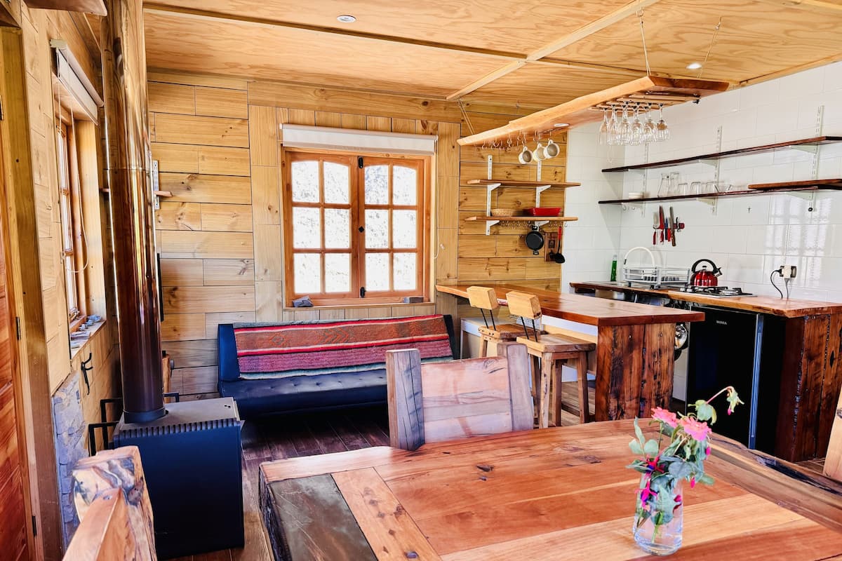 Un intérieur en bois comprenant une table à manger, un banc et un coin cuisine avec un poêle.
