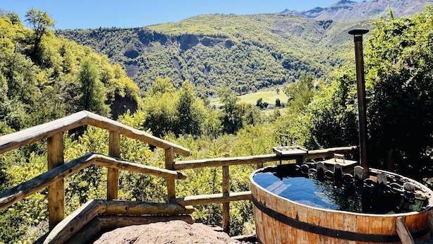A wooden deck with a hot tub and a wooden railing overlooking a mountainous landscape.