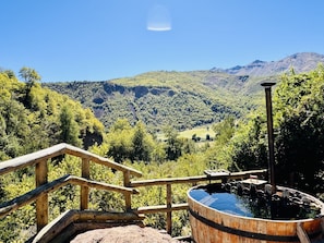 A wooden deck with a hot tub and a wooden railing overlooking a mountainous landscape.
