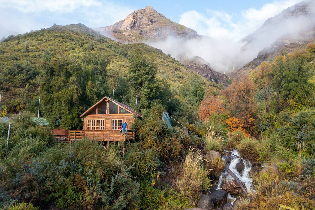 Une cabane en bois dotée d’une terrasse en bois, entourée d’une végétation luxuriante et avec une chaîne de montagnes en toile de fond.