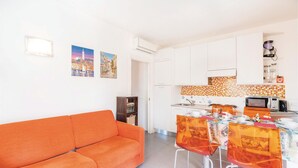 Eine moderne Küche mit weißen Schränken, einer Mikrowelle und einer Kaffeemaschine. Es gibt einen Esstisch mit Stühlen und ein Sofa im Wohnbereich.
