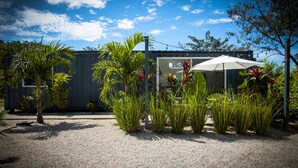 Un edifici modern amb sòl de grava, envoltat de diverses plantes i un parasol gran.