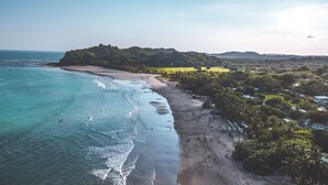 Vista aèria d'una platja amb aigües turqueses cristal·lines, sorra daurada i vegetació exuberant.