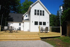 A white two-story house with a wooden deck and outdoor seating area.