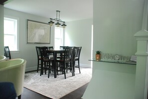 A dining area with a round table and chairs, a chandelier, a map on the wall, and a welcome sign on a shelf.