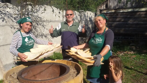 Trois personnes portant des tabliers et tenant du pain, avec un grand saladier en bois au premier plan.