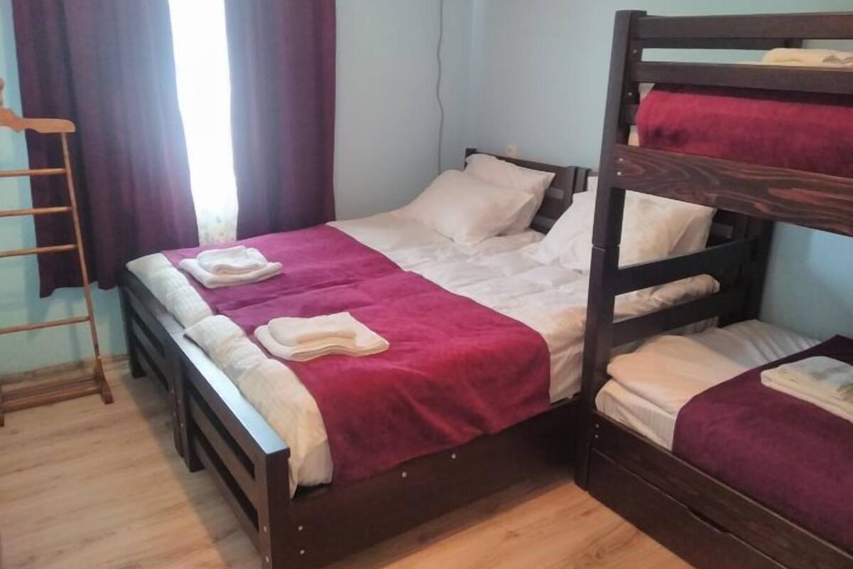 A dormitory room with bunk beds, a wooden floor, and a window with curtains.
