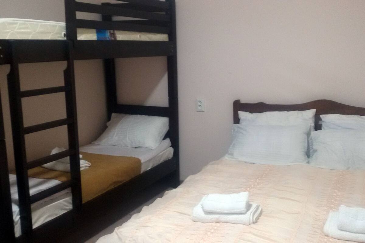 A bunk bed room with a wooden headboard, a single bed with a beige bedspread, and two rolled-up towels on the bed.