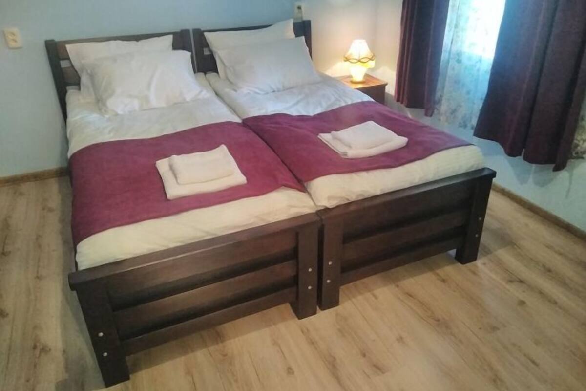 A double bed with two pillows and a blanket, a bedside table with a lamp, and a window with curtains.