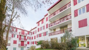 Un edificio residencial de varios pisos con balcones, un césped verde y un árbol.