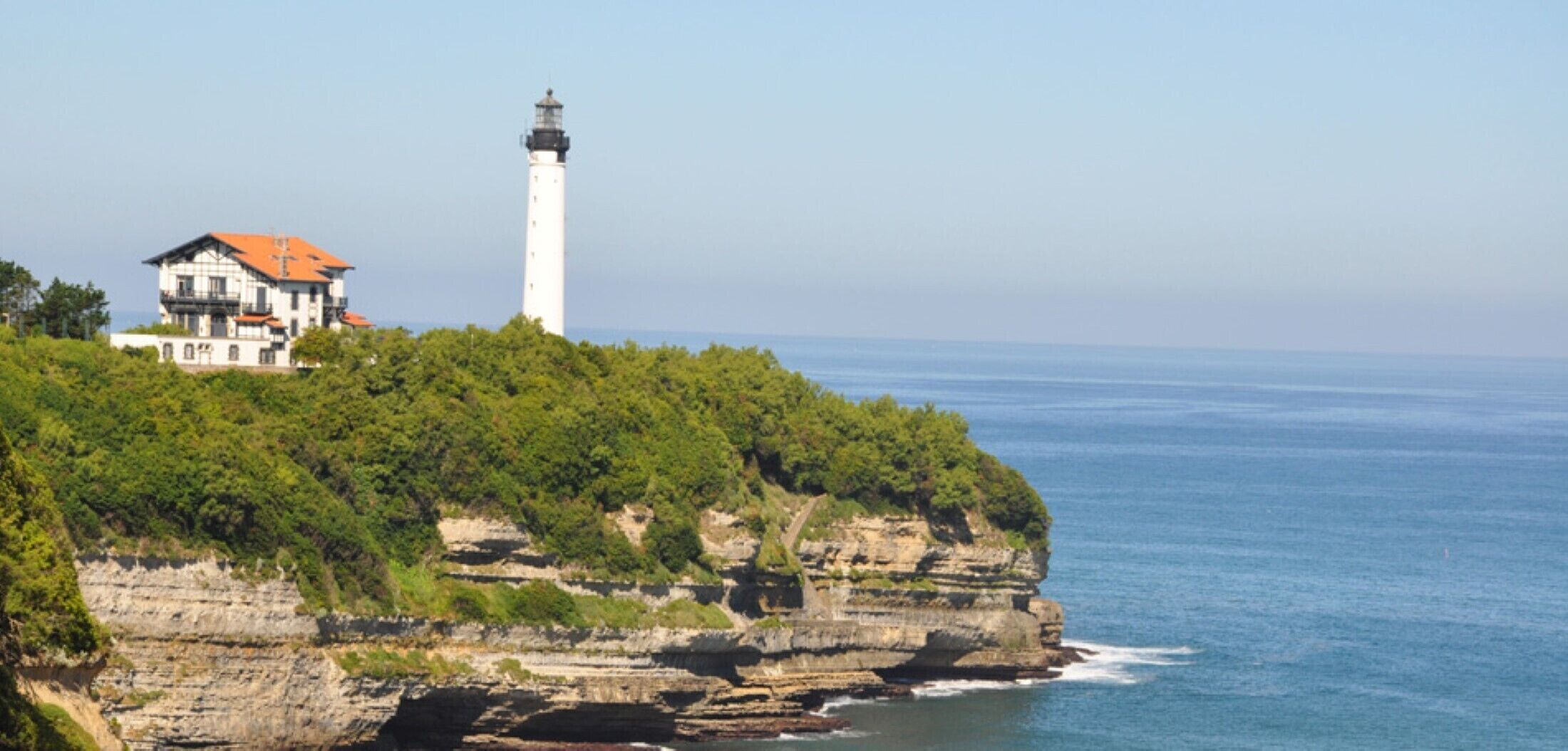 A coastal house with a lighthouse on a cliff overlooking the sea.