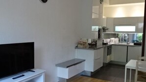 Una sala de estar moderna con un televisor de pantalla plana, un pequeño banco blanco y una cocina con armarios y una encimera.