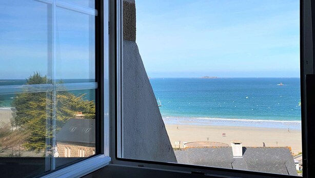 Une vue depuis une fenêtre donnant sur une plage, avec un ciel dégagé.