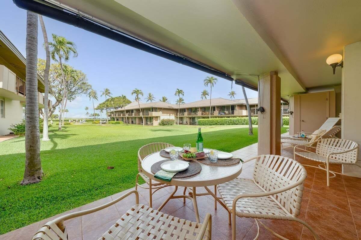 Un balcon avec des fauteuils en osier, une table dressée pour le repas, et une vue sur une pelouse bien entretenue et des bâtiments en arrière-plan.
