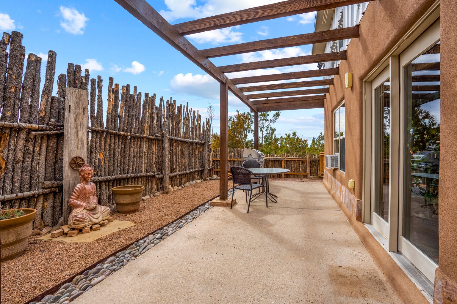 Un patio abrité, agrémenté d’une clôture en bois rustique, d’une statue de Bouddha et d’une table avec des chaises.