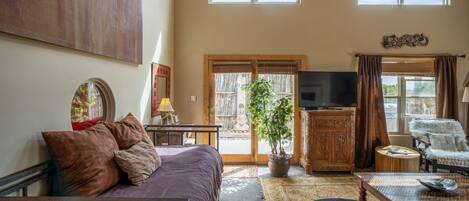 A spacious living room with a sofa, a television, a dining table, and a large window.