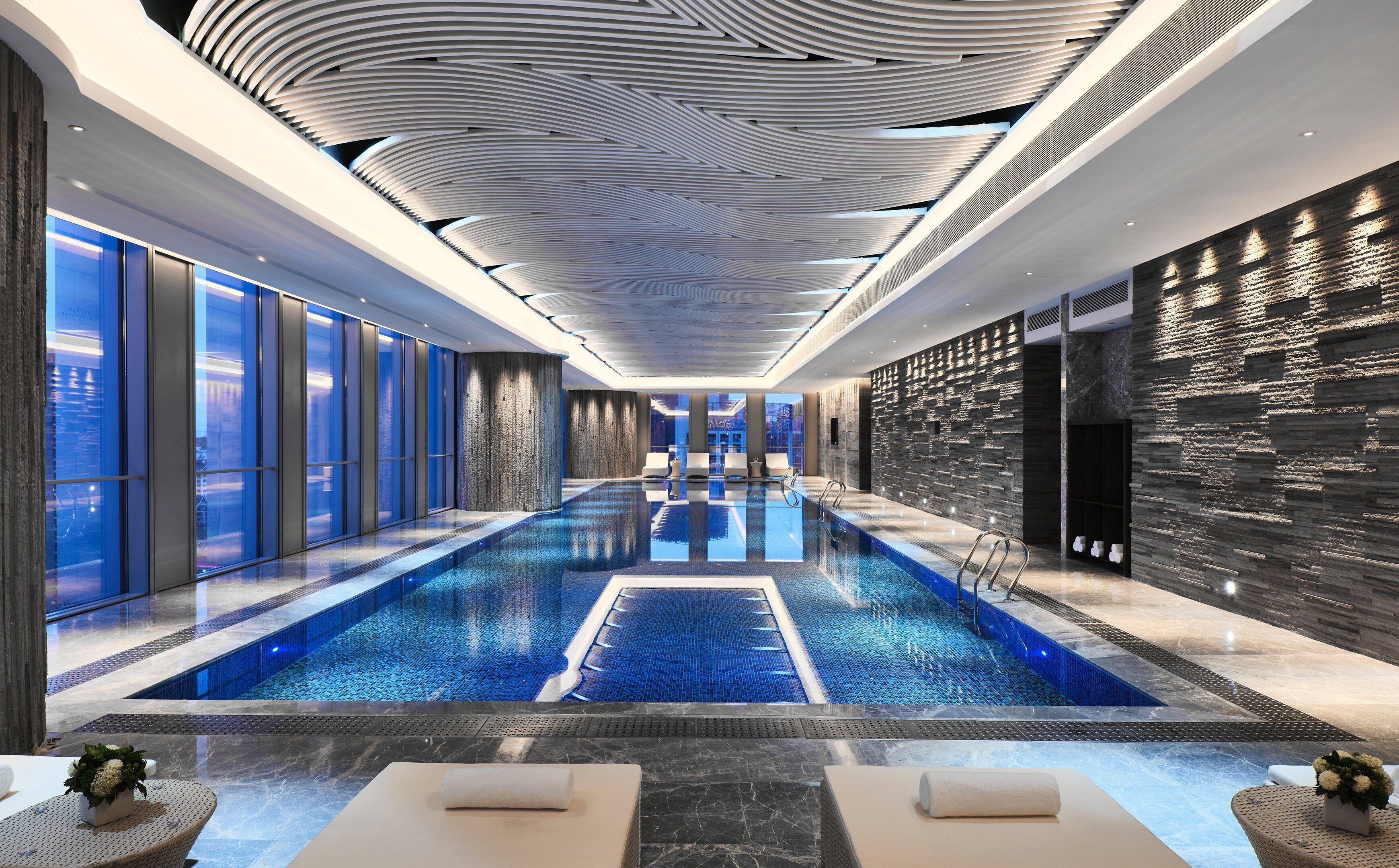 A modern indoor swimming pool with a clear view of the cityscape through large windows.