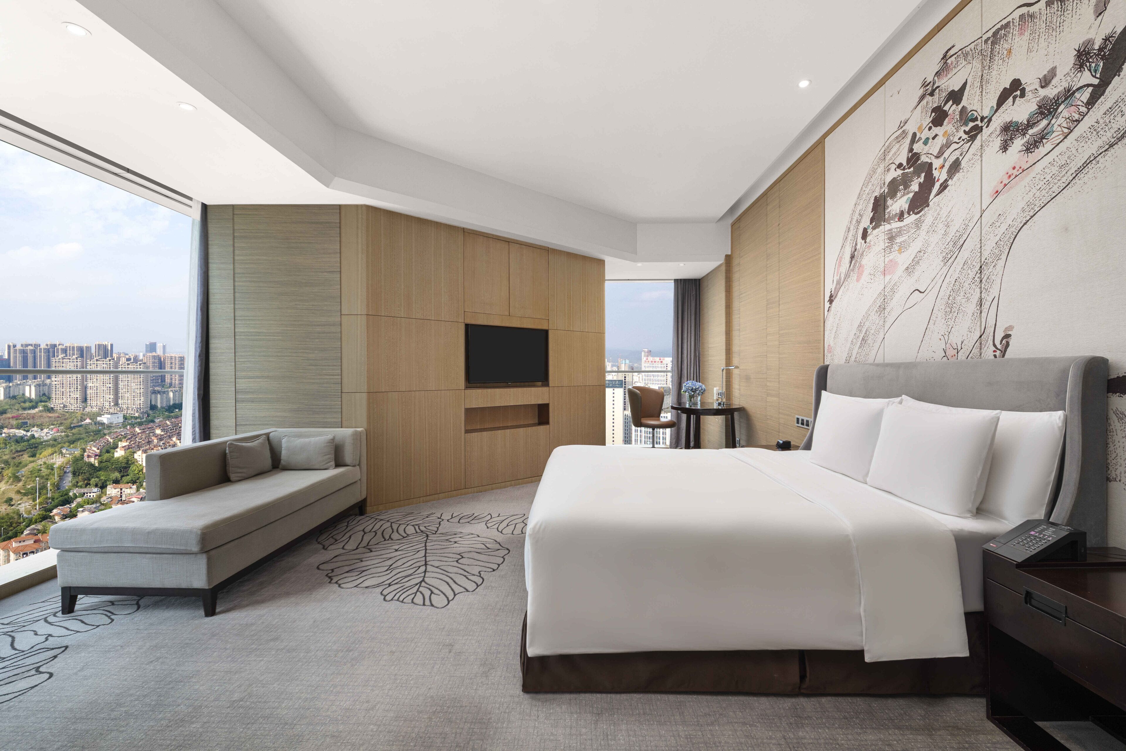 Habitación de hotel moderna con una cama grande, un sofá, un televisor de pantalla plana y vistas a la ciudad.