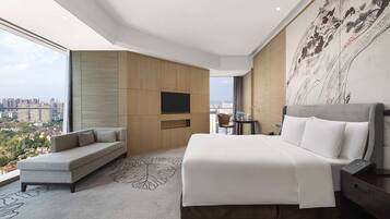 Habitación de hotel moderna con una cama grande, un sofá, un televisor de pantalla plana y vistas a la ciudad.
