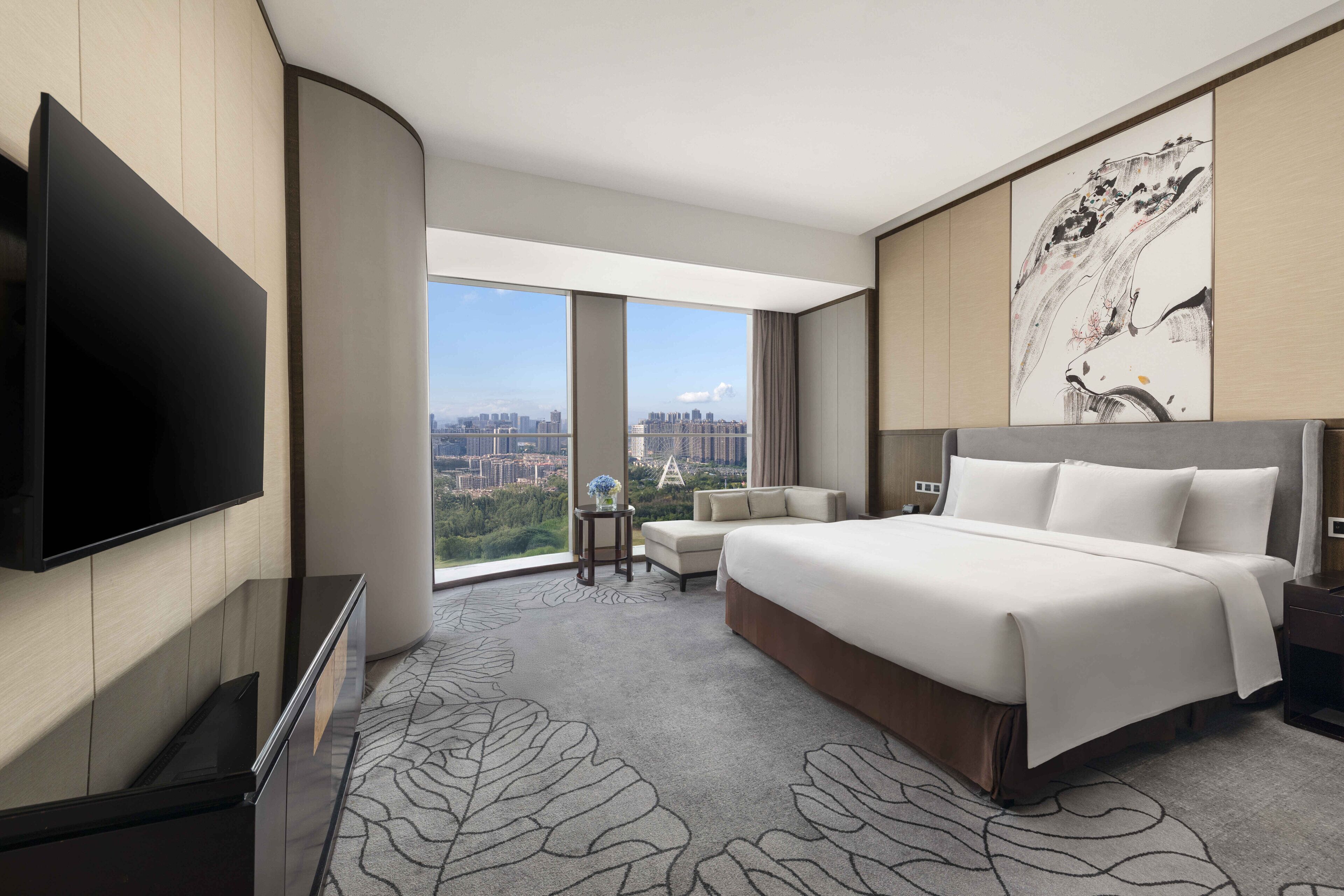 Una habitación de hotel moderna con una cama grande, un televisor de pantalla plana, vista a la ciudad y un elemento decorativo en la pared.