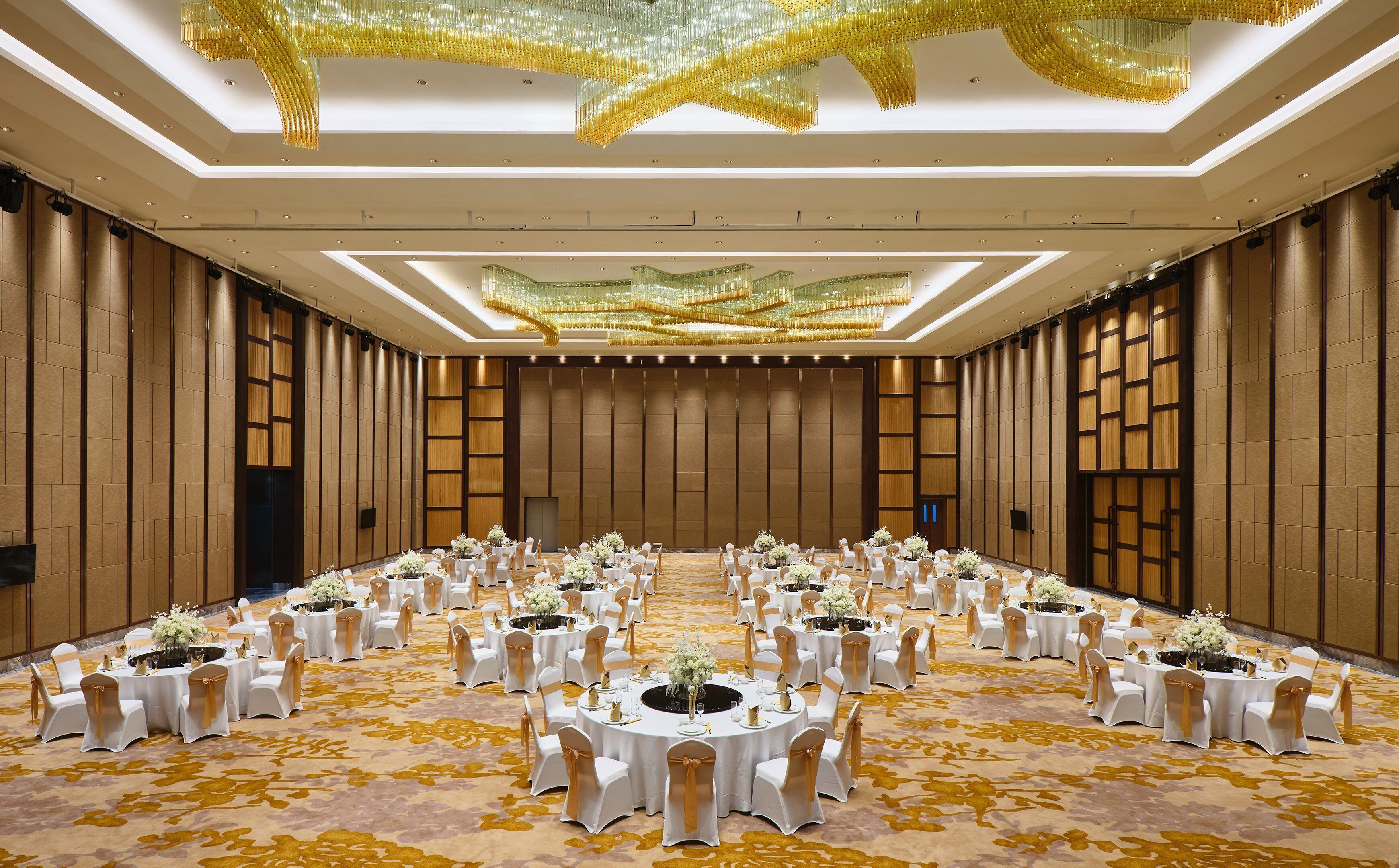 Une vaste salle de banquet avec des tables rondes, des nappes blanches et des rubans dorés.