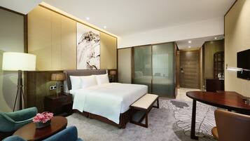 A hotel room with a bed, bedside table, lamp, chair, bench, and a TV.