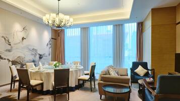 A dining area with a round table set for six, surrounded by chairs, a chandelier, and a large window with curtains.