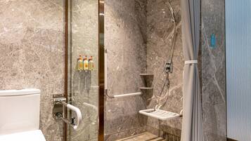 A modern bathroom with a glass-enclosed shower, a toilet with grab bars, and a shelf with toiletries.