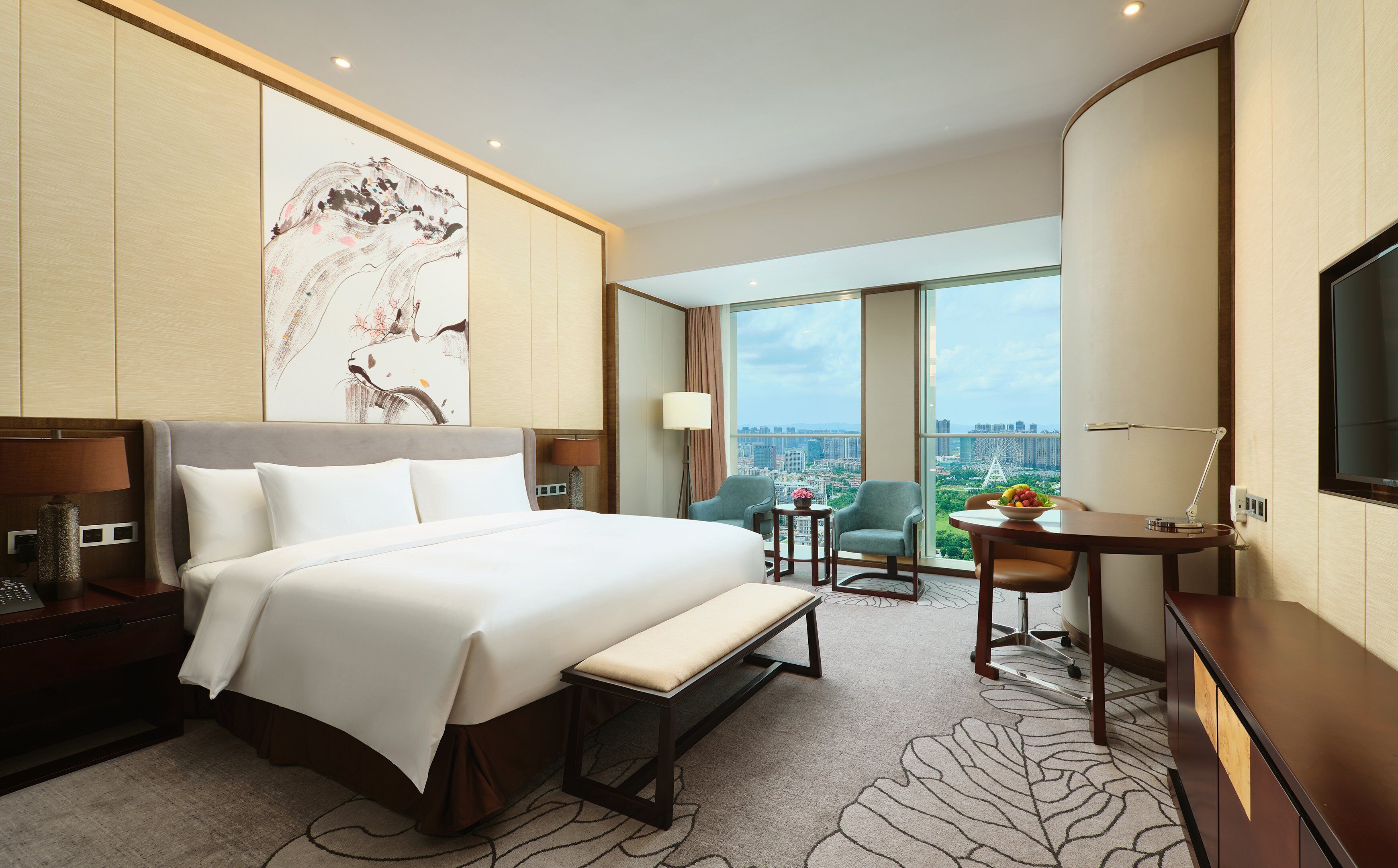 A hotel room with a large bed, a desk, a chair, a TV, and a view of a cityscape.