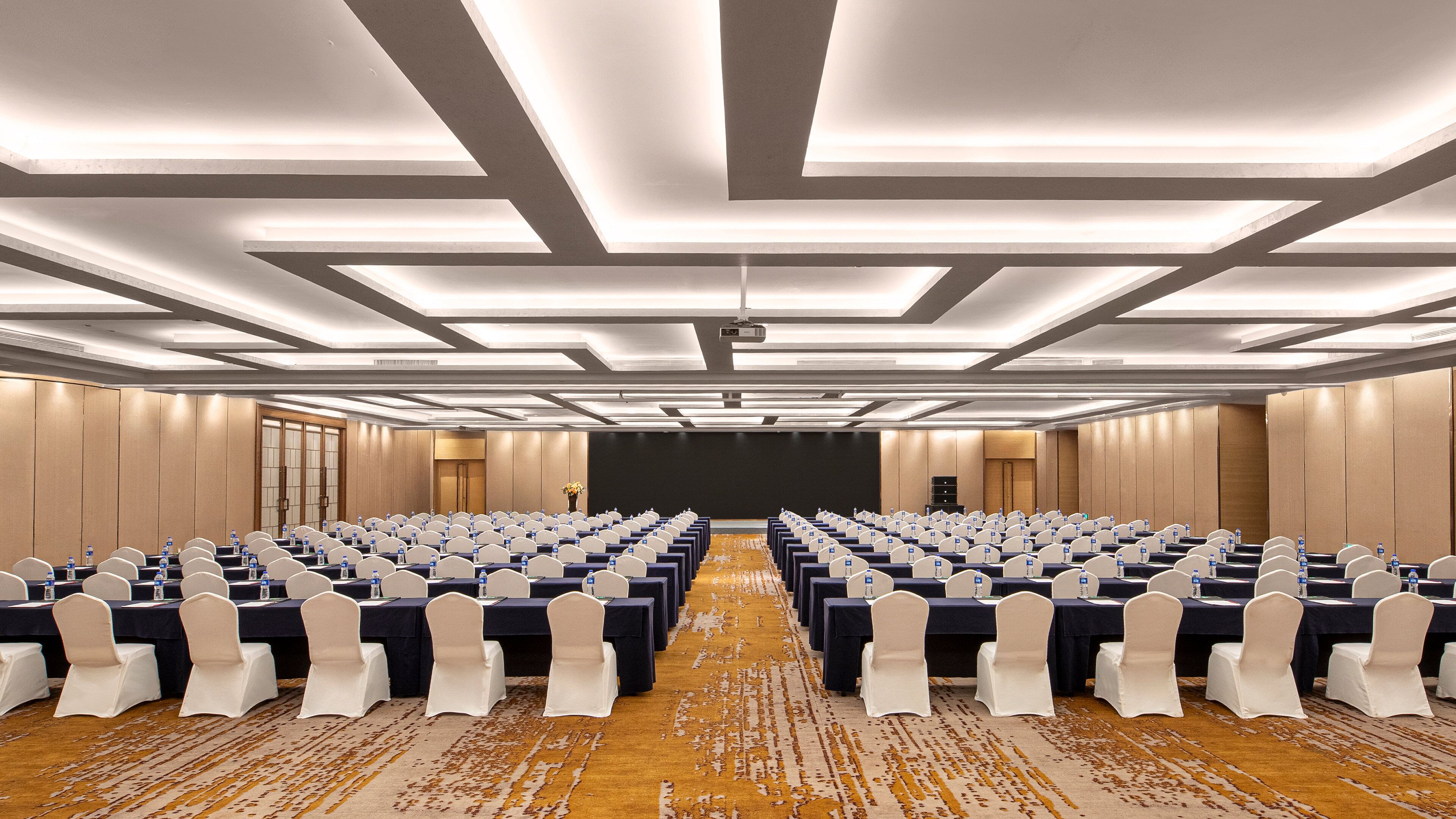 A conference room with rows of tables, chairs, and a projector screen.