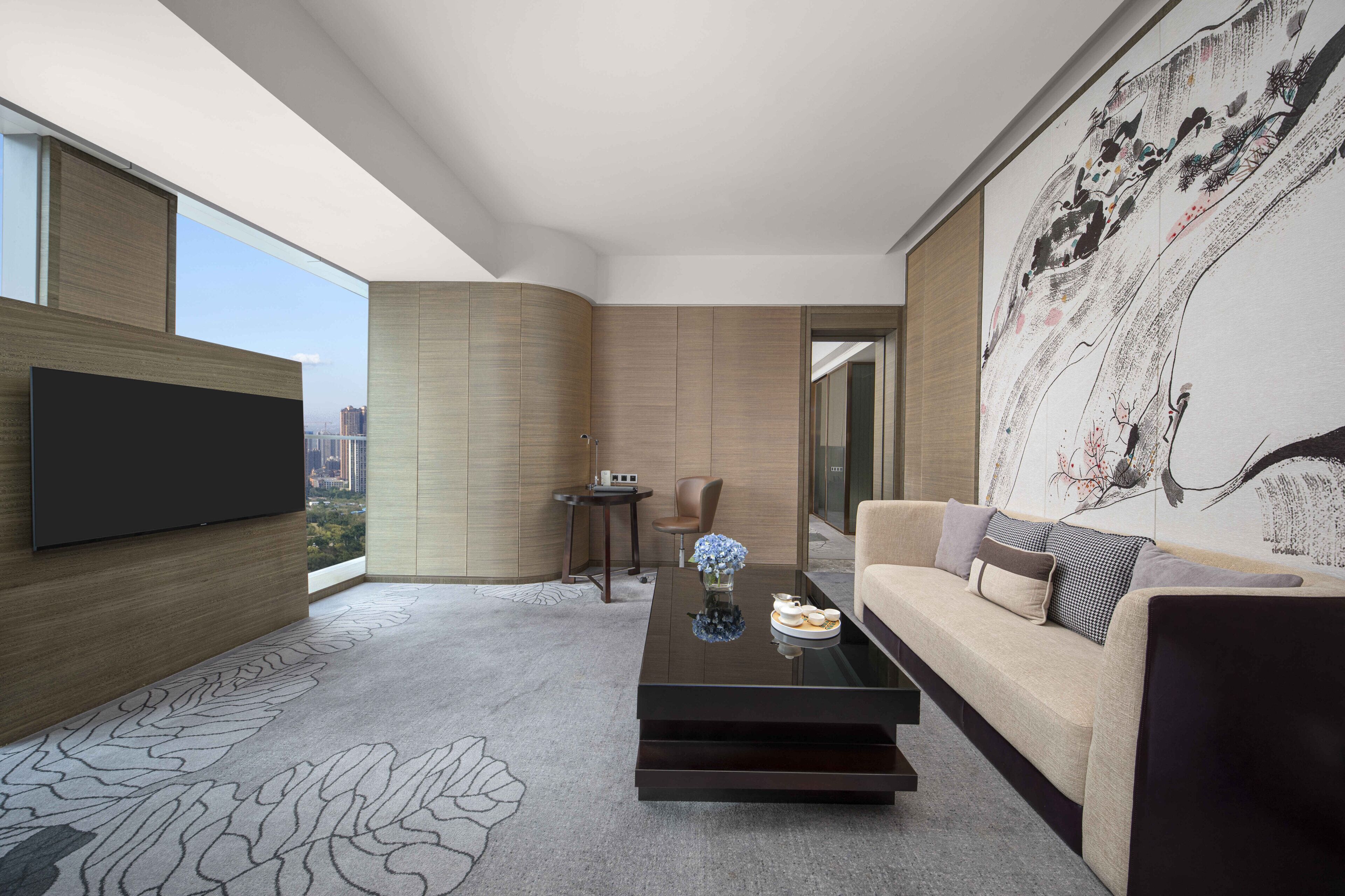 A modern living room with a flat-screen TV, a sofa, a coffee table, and a large painting on the wall.