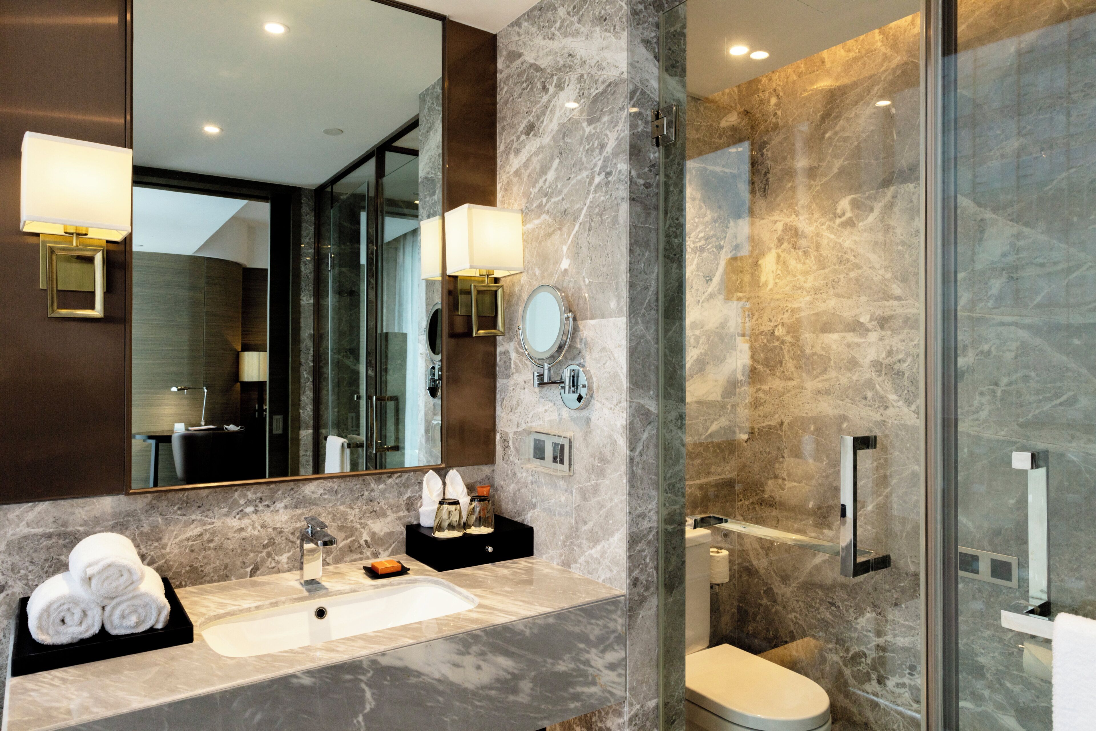 Une salle de bain moderne avec un lavabo en marbre, un grand miroir et une douche à parois de verre.
