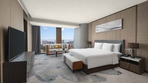 Una habitación de hotel moderna con una cama grande, un televisor de pantalla plana, un sofá, una mesa de centro y vistas a la ciudad.