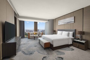 Una habitación de hotel moderna con una cama grande, un televisor de pantalla plana, un sofá, una mesa de centro y vistas a la ciudad.