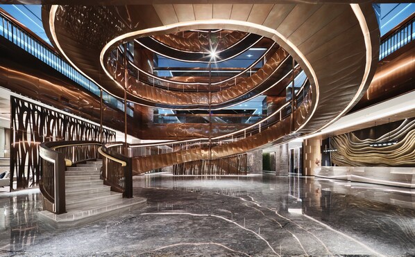 A modern interior with a central spiral staircase, polished marble floors, and a high ceiling.