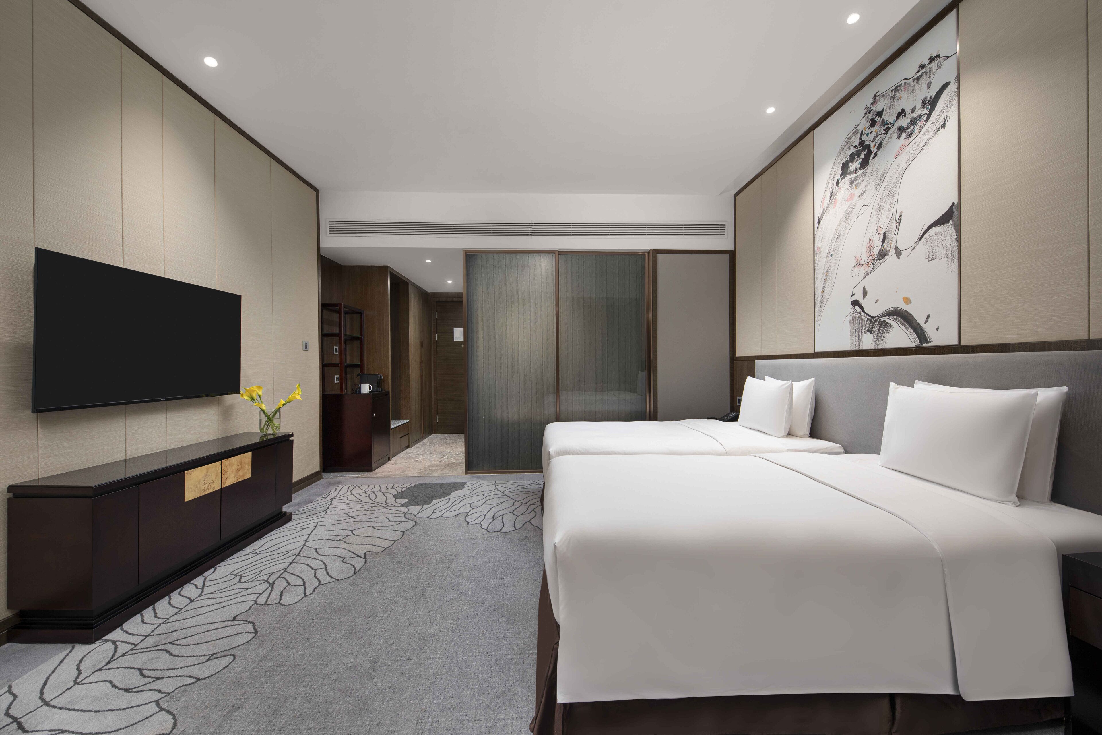 Een moderne hotelkamer met een groot bed, een flatscreen televisie, een donkere houten console en een groot kunstwerk aan de muur.