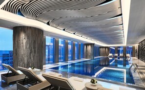 A modern indoor pool area with lounge chairs and a view of the cityscape.