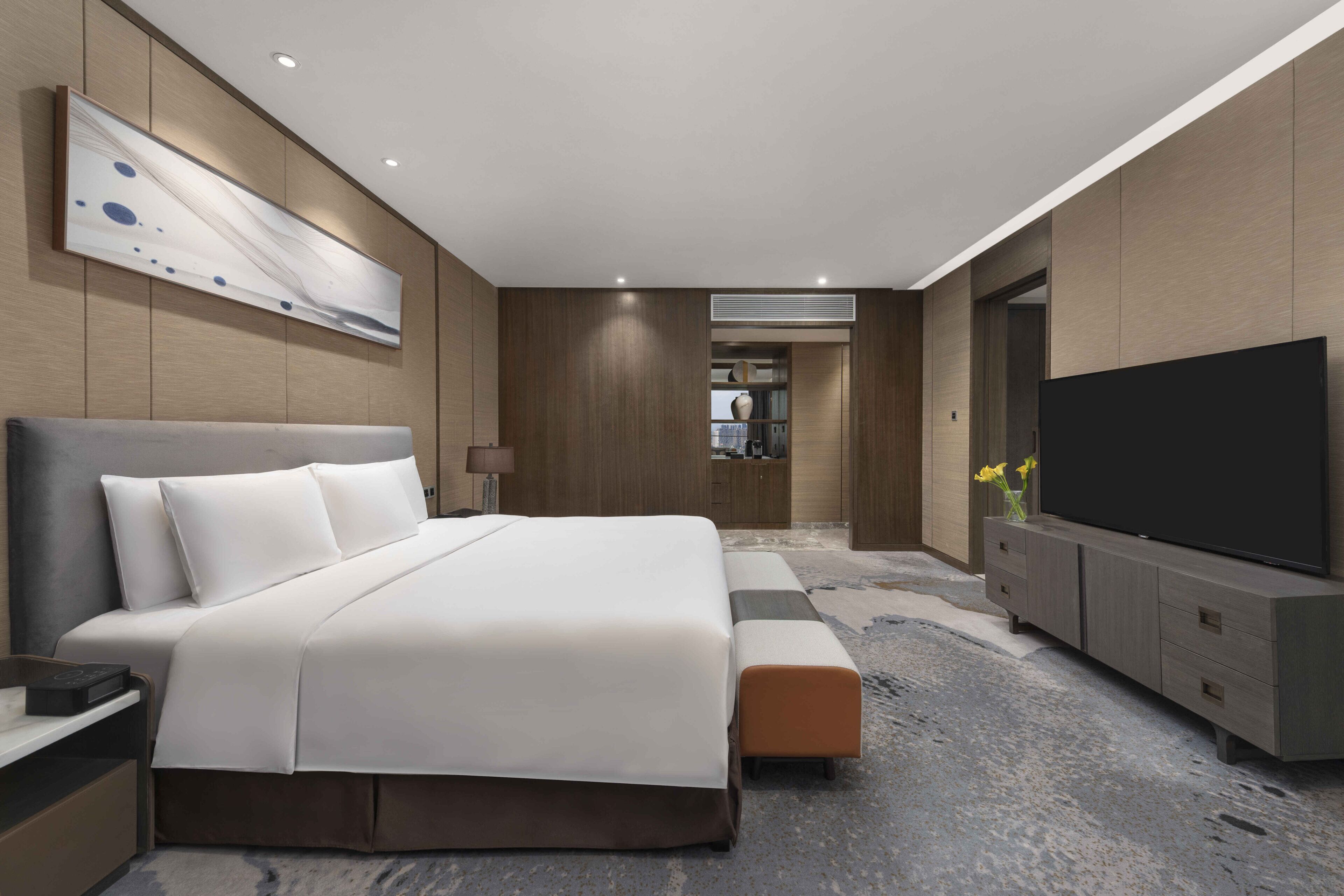 A modern hotel room with a large bed, a flat-screen TV, a built-in wardrobe, and a large abstract painting on the wall.