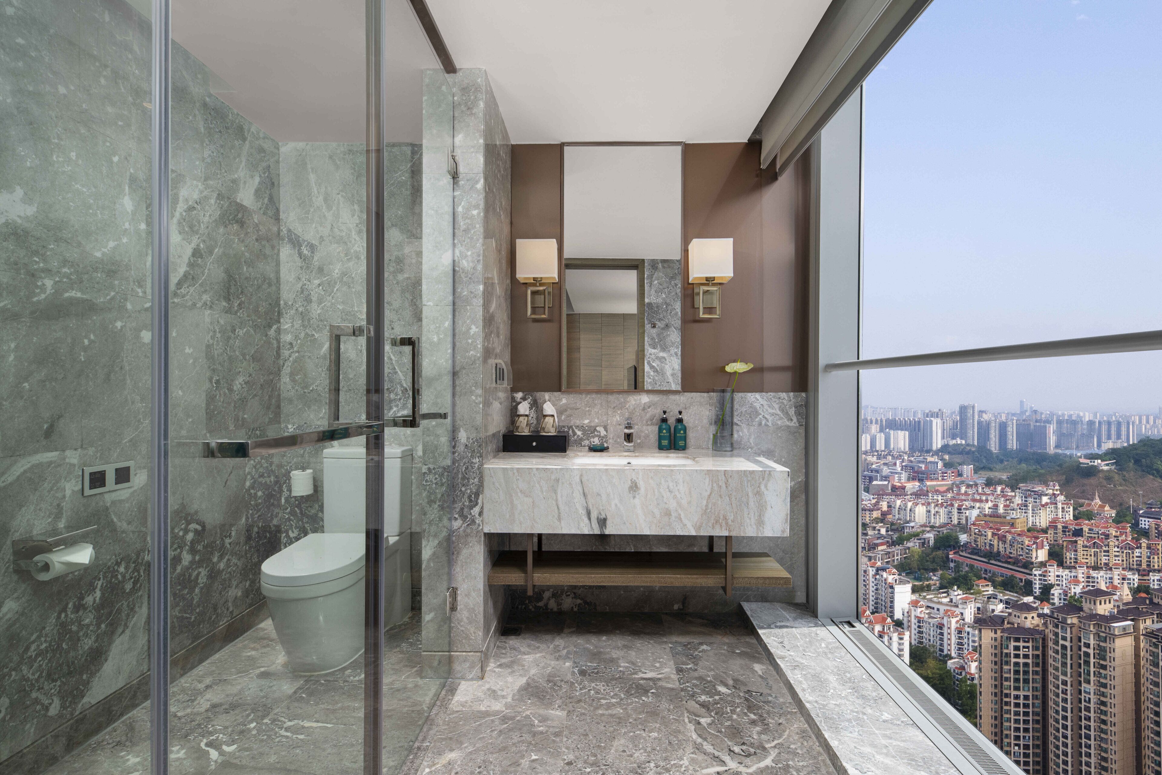 A modern bathroom with a glass shower enclosure, a marble sink, and a cityscape view.