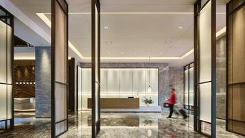 A modern lobby with a reception desk, marble flooring, and a person walking through the space.