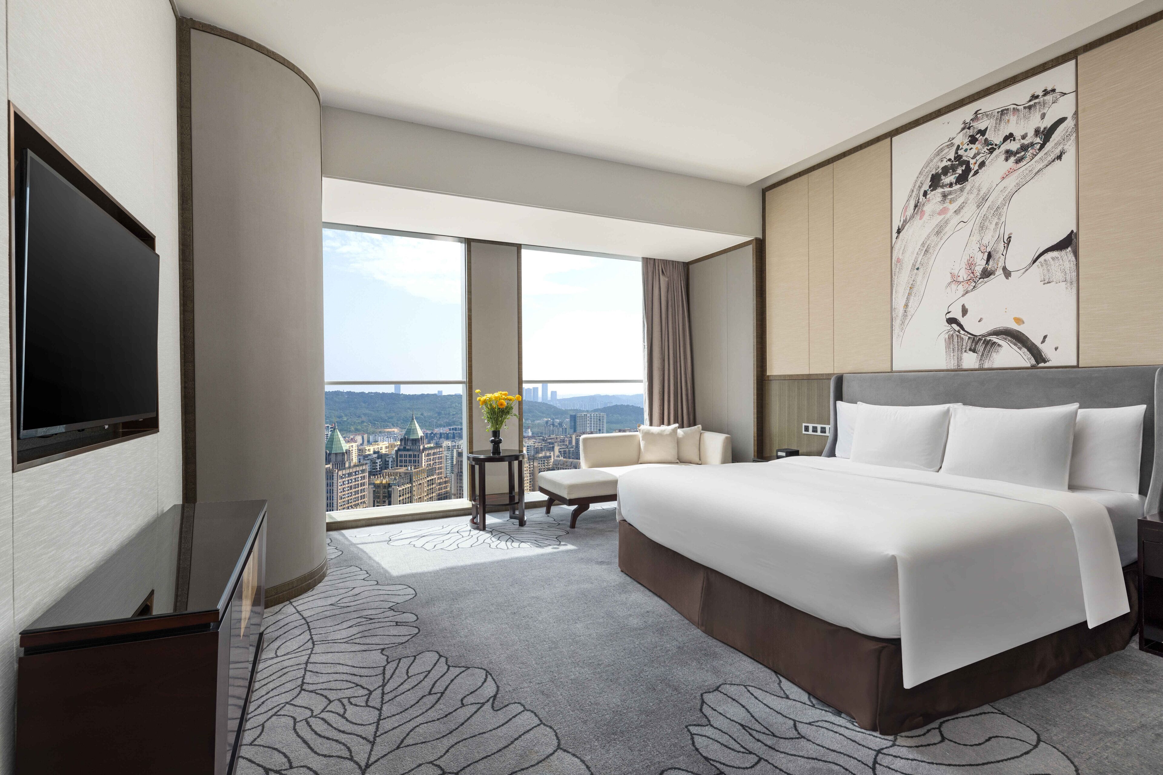 Une chambre d’hôtel avec un grand lit, une télévision, une vue sur la ville et un élément décoratif mural.