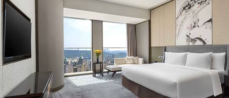 Habitación de hotel con una cama grande, televisión, vista a la ciudad y un adorno en la pared.