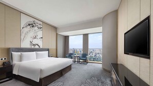 Habitación de hotel con una cama grande, televisión, escritorio con teléfono, una silla y vista a la ciudad.