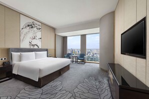 Habitación de hotel con una cama grande, televisión, escritorio con teléfono, una silla y vista a la ciudad.