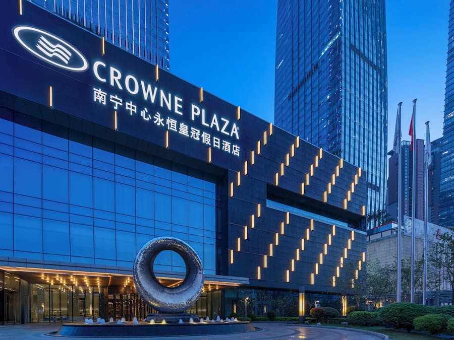 A modern building with a sign reading 'CROWNE PLAZA' and a large circular sculpture in front.