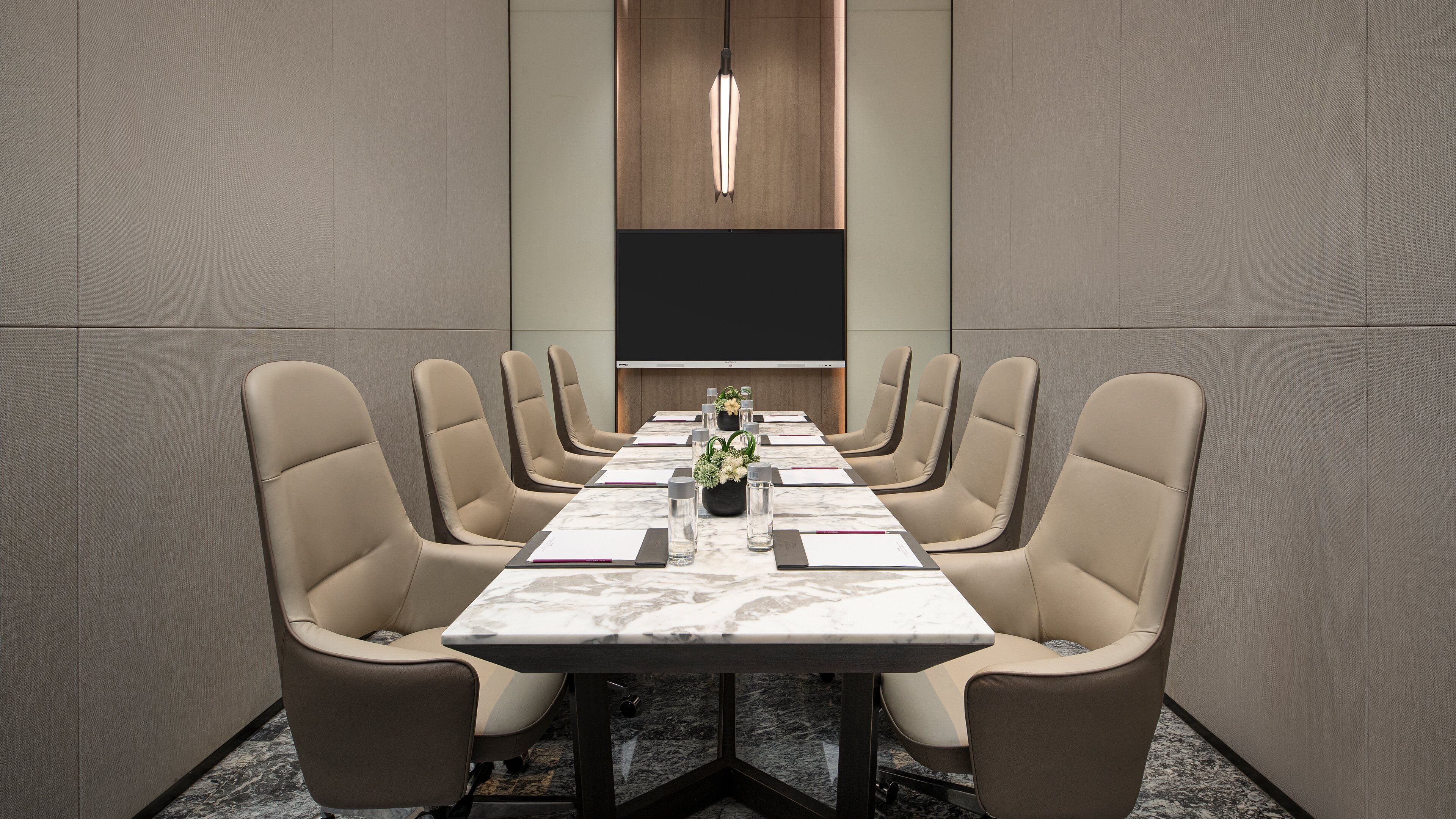 A conference room with a long table, beige chairs, a marble table top, and a plant centerpiece.