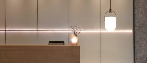 A reception desk with a wooden finish, a vase with branches, and a wall-mounted light fixture.